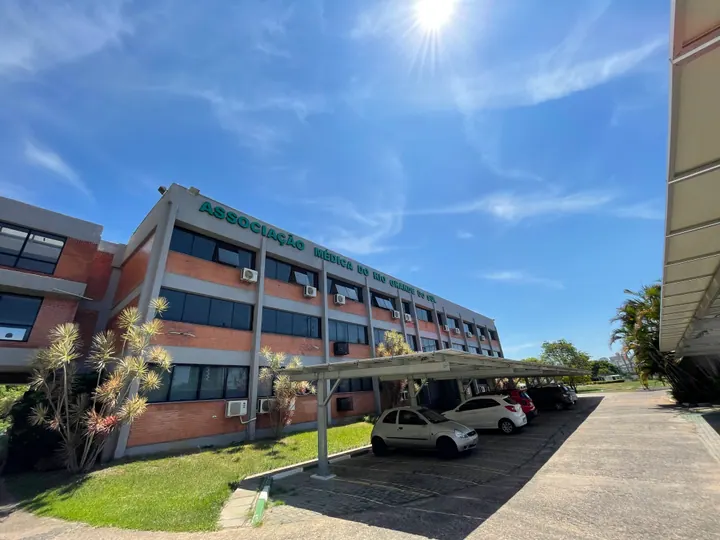 Fachada da sede da AMRIGS em Porto Alegre, com o nome da associação no edifício e céu azul