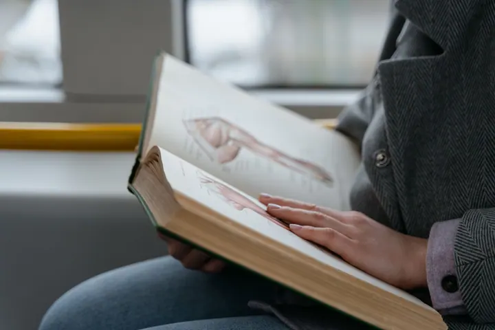 Mãos seguram um livro aberto com ilustrações dos músculos da perna