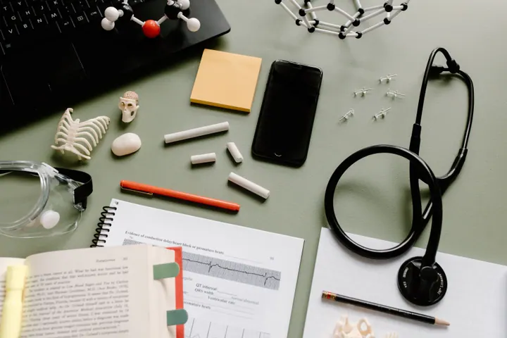 Mesa com computador, livros médicos, caderno, modelos anatômicos e estetoscópio