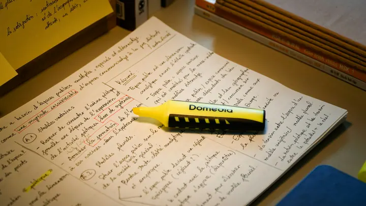 Marca-texto amarelo sobre páginas de anotações manuscritas, com trechos destacados e livros de estudo ao fundo