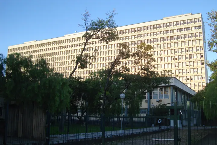 Edifício do Hospital de Clínicas de Porto Alegre, com longas faixas de janelas, árvores e céu azul