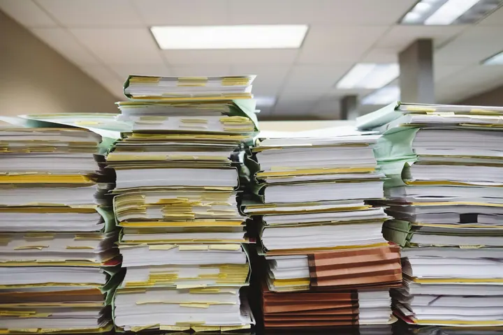 Pilhas de documentos em pastas com marcadores amarelos em um ambiente de escritório
