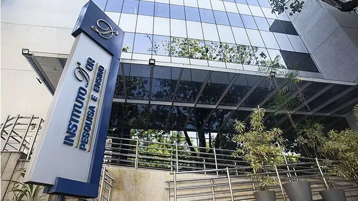 Fachada de vidro e entrada da Unidade Botafogo do Instituto D’Or de Pesquisa e Ensino, com totem identificando o instituto
