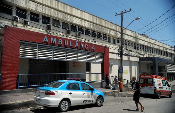 Entrada e fachada do Hospital Estadual Getúlio Vargas, com ambulância e veículos em frente ao prédio.